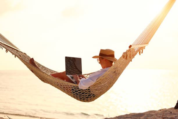 istock Young woman female freelancer using laptop while lying in hammock on the tropical beach at sunset 1334750739