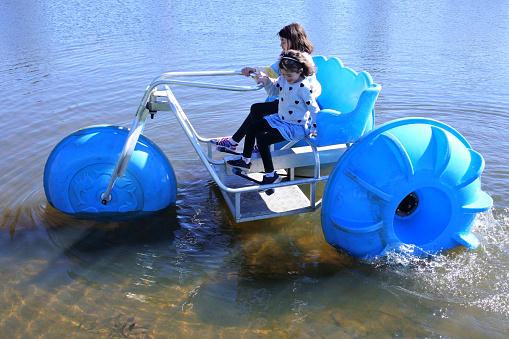 Aerial view of two young girls sisters (age 11-12 and 7-8) riding on a big wheel aqua bike water tricycle  over a lake waters.