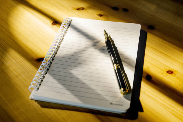 istock Close-up notebook and pen on wooden table with sun shining, light and shadow 1334755123
