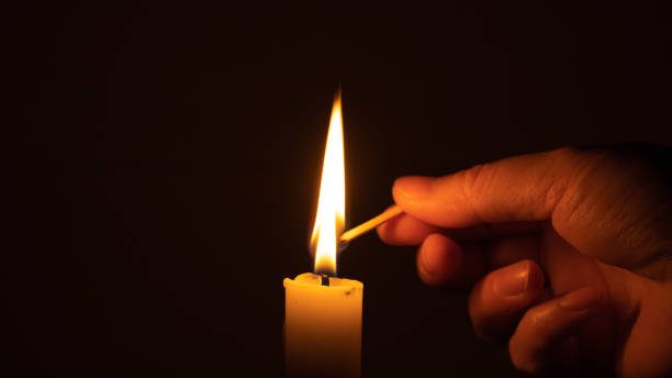 istock At the dark night, a hand holding a lighted match and lighting a white candle 1334763402