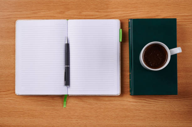 istock Plain Blank Notebooks And A Pen Beside A Cup Of Coffee Placed Book Table. Simple Empty Notepads With A Ballpen And Mug Over Dictionary Desk. 1334768549