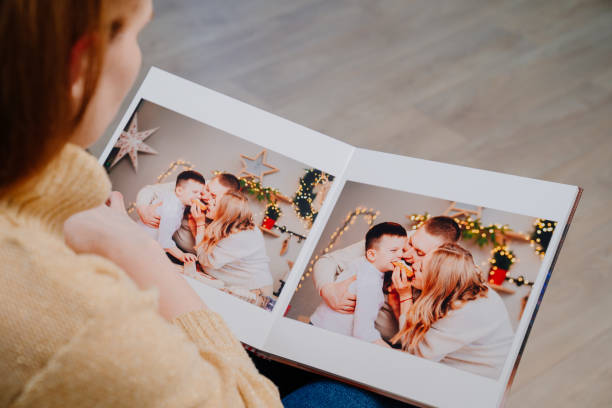 frau blättert durch die seiten des fotobuchs von einem familienfotoshooting in der küche - ausdrucken fotos stock-fotos und bilder