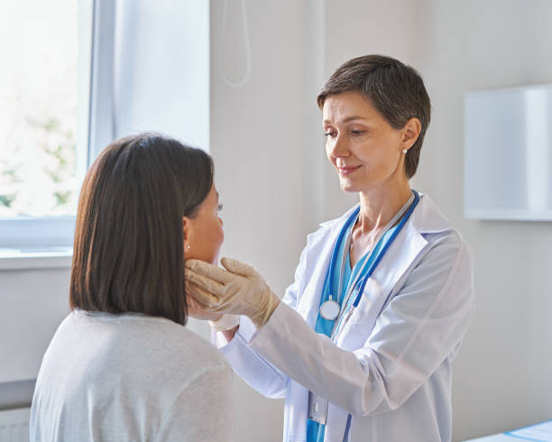 Middle-aged woman doctor wearing gloves checking patients sore throat or thyroid glands stock photo