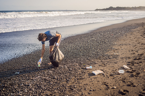 Young man cleaning up the beach. Natural education of children.