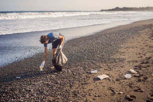 jovem limpando a praia. educação natural das crianças - mulher catando lixo - fotografias e filmes do acervo