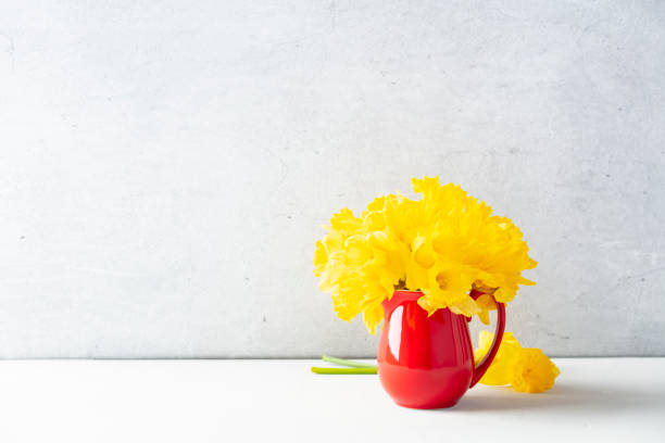 Bouquet of yellow daffodils in a red jug on table top, home decor, interior, copy space