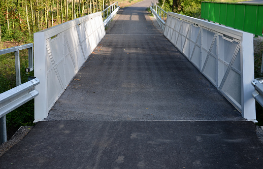 path for cyclists with an asphalt surface. galvanized iron railing over road barriers. Bridge railing with tilting to the sides. railing made of perforated sheet metal in the shape of a triangle, expansion joint, dilatation