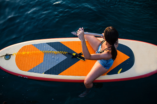 A young woman is sitting on a SUP board paddling at the seaside