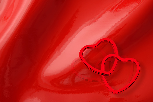 High angle view of two red heart shaped rings on shiny red vinyl background with copy space.