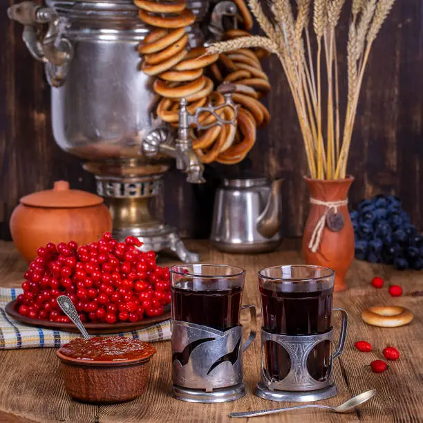 Russian traditional kettle samovar on the wooden table. Black tea, bagels, red viburnum, jam and tea samovar in the rustic style. Russian national tea ceremony