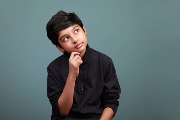 little boy of indian ethnicity looking up and thinking - facial expression child asia asian and indian ethnicities imagens e fotografias de stock