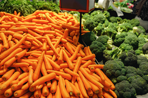 Pile of fresh carrots and broccoli on counter in supermarket, close up