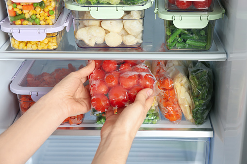 Mujer tomando bolsa de plástico con tomates congelados del refrigerador, primer plano photo