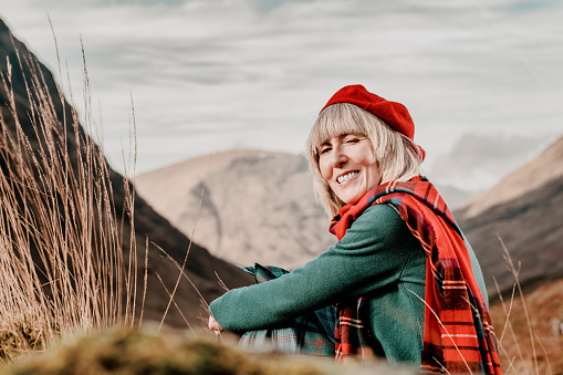 Mature woman in green wool sweater, tartan scarf and red beret, in Glencoe, Scotland.