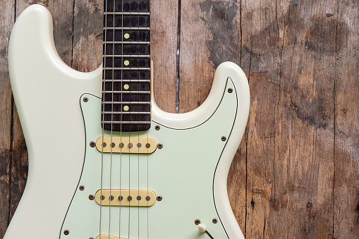 Detail of White Electric Guitar on a wood background.