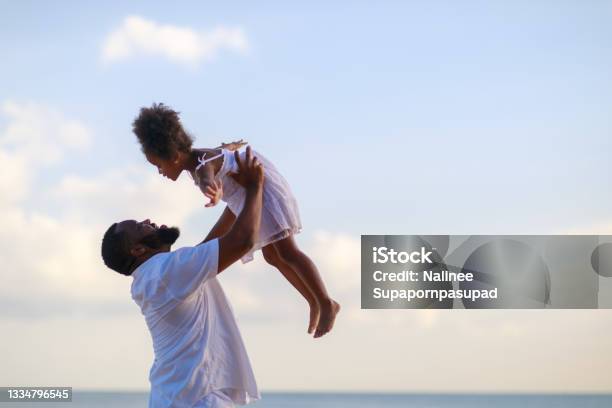 Smiling African American father carrying little daughter on beach during holiday time.