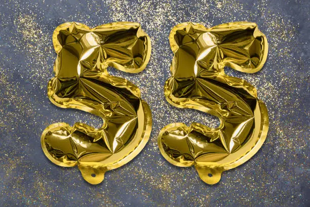 Photo of The number of the balloon made of golden foil, the number fifty-five on a gray background with sequins.