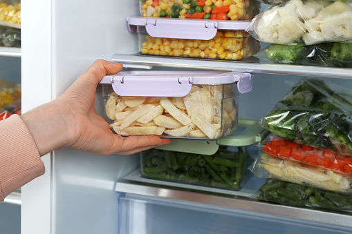 Woman taking container with frozen potato from refrigerator, closeup