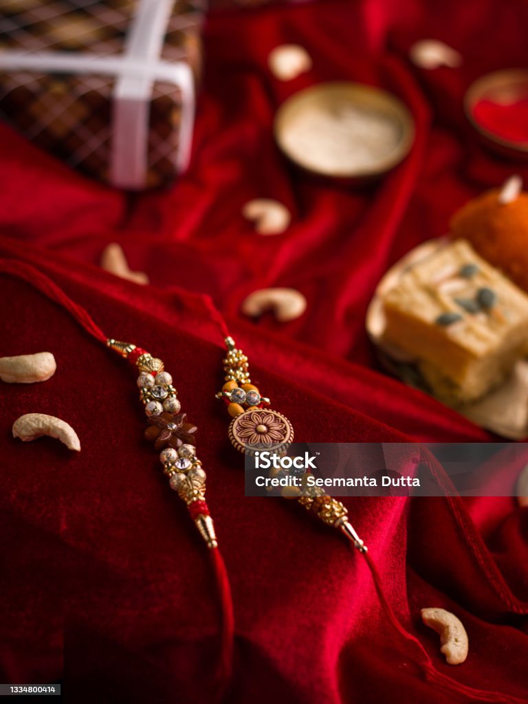 Raksha Bandhan background with an elegant Rakhi and Rice Grains on red cloth textured background. Rakhi Stock Photo