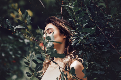 Portrait of a young beautiful model girl among the leaves of a tree in nature