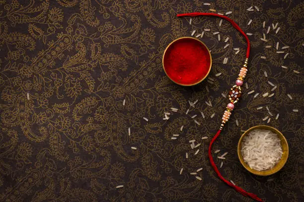 Raksha Bandhan background with an elegant Rakhi and Rice Grains on dark textured background.