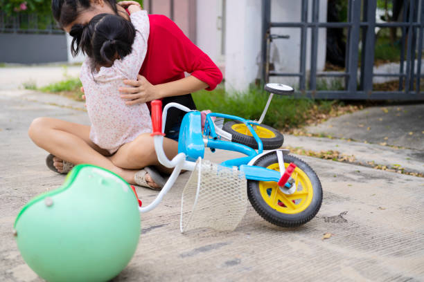 criança se machucando enquanto andava de bicicleta. mãe ajudando sua filhinha - acidente evento relacionado com o transporte - fotografias e filmes do acervo