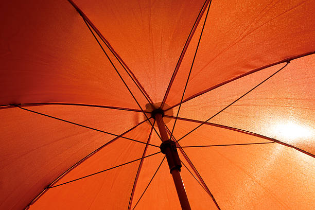 Orange umbrella from underneath with sun shining through stock photo