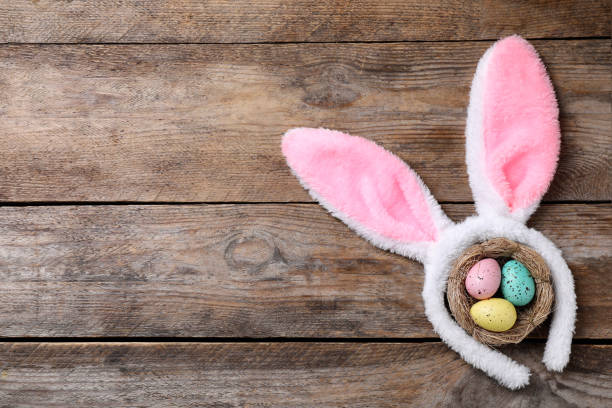 istock Headband with bunny ears, painted eggs and space for text on wooden background, flat lay. Easter holiday 1334802830