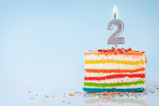 Birthday cake with number two candle on a blue background with copy space for your greetings