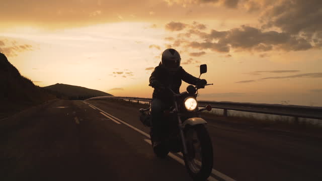 Silhouette of single driver riding motorbike on mountain highway against sunset in slow motion
