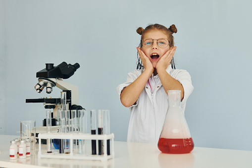 Scared little girl in coat playing a scientist in lab by using equipment.