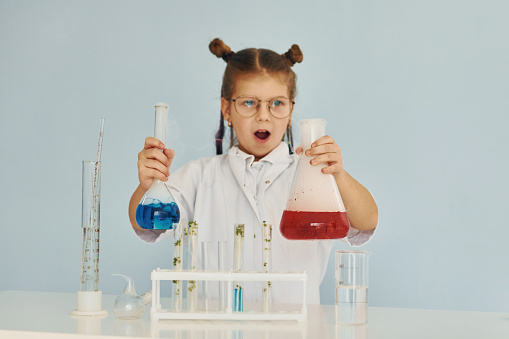 Scared little girl in coat playing a scientist in lab by using equipment.