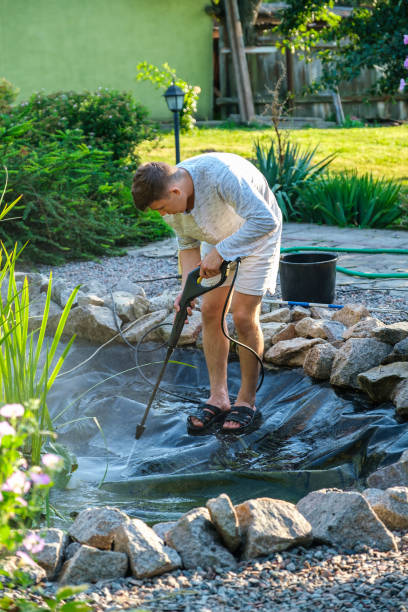istock man cleans garden pond bottom with high-pressure washer from mud and sludge. 1334817874