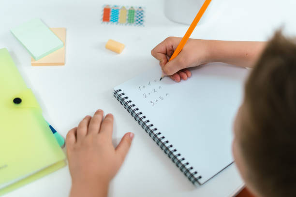 istock Distance learning online education. Kid boy studying at home with book, writing in notepad and doing school homework. Child siting at table with notepad. solve mathematical problems. Back to school 1334819307