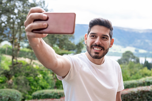 Latin man of average age of 25 years dressed informally in the middle of nature takes a selfie with his mobile phone