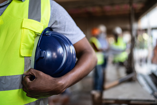 Midsection of a construction worker holding hardhat