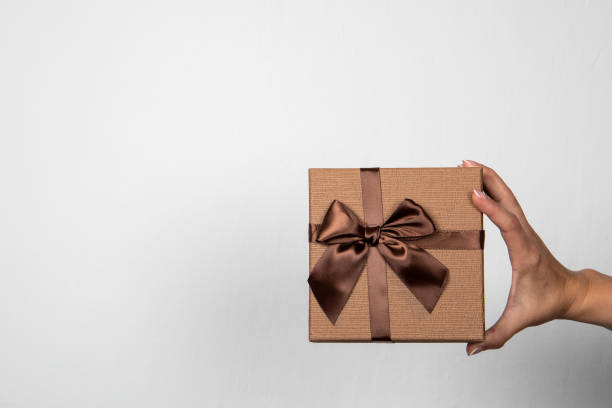 istock Brown gift box in a woman's hand on a light background 1334823174