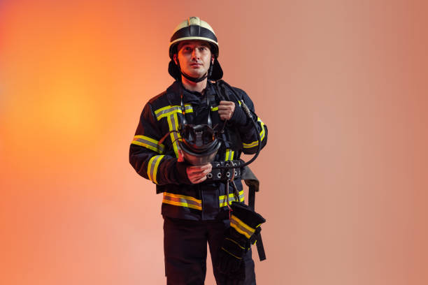 istock One male firefighter dressed in uniform posing over orange background in neon lights. 1334826159