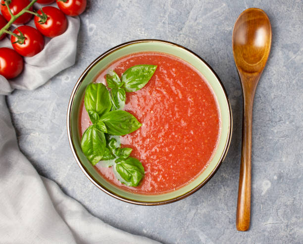 가스파초와 바질 그린 잎이 있는 그릇의 최고 전망. 나무 숟가락과 체리 토마토 의 잔가지와 콘크리트 표면에 토마토 수프 - tomato soup red basil table 뉴스 사진 이미지