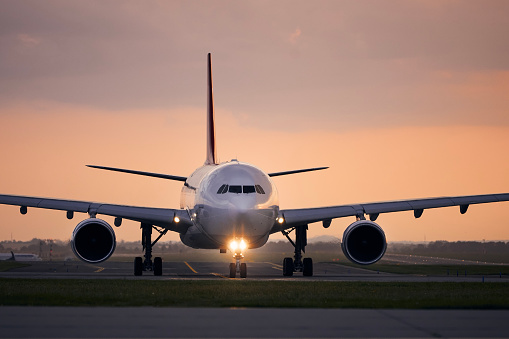 Wide-body airplane taxiing for take off. Front view of plane against airport at sunset.\