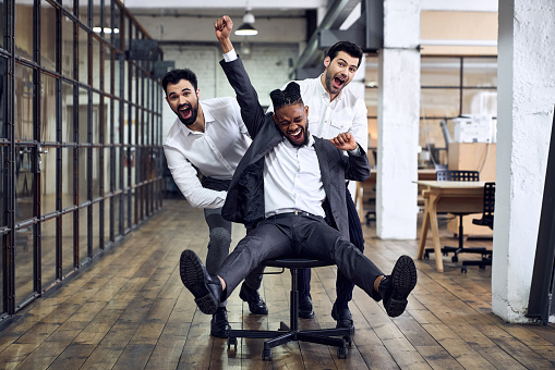 Trabajar duro jugar duro. Cuatro jóvenes empresarios alegres con ropa formal divirtiéndose mientras corrían en sillas de oficina y sonreían. photo