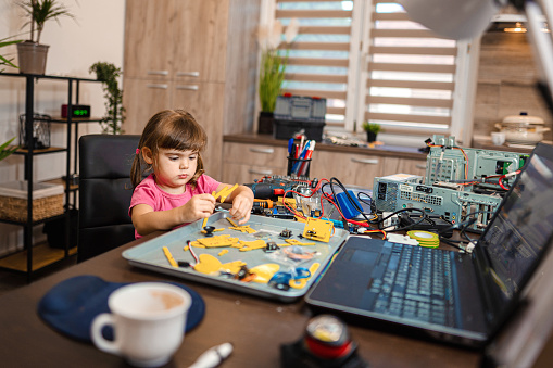 Happy little girl soldering mother board during school science project