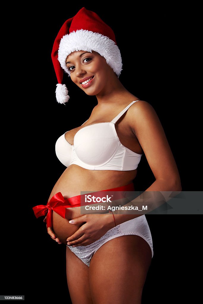 Christmas gift. Pregnant woman in underwear and santa hat, against black. Abdomen Stock Photo