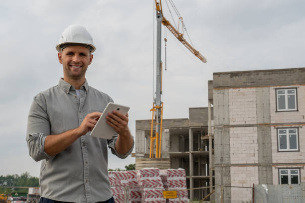 istock Construction engineer in a white helmet with a yellow crane in the background uses a tablet 1334837350