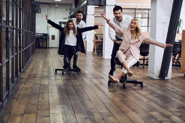istock Work hard play hard. Four young cheerful business people in formal wear having fun while racing on office chairs and smiling 1334837591