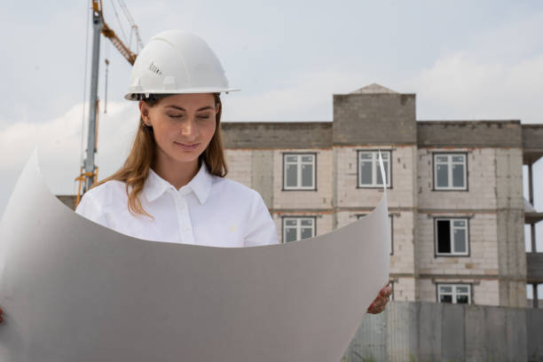 istock Female construction worker in a white helmet holds drawings on a construction site 1334838558