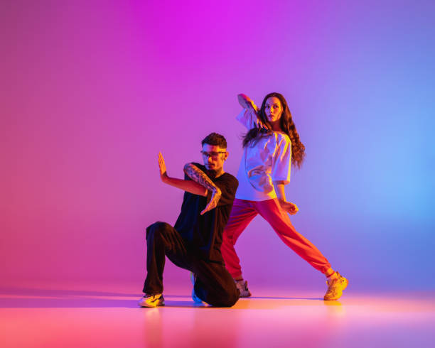 カジュアルな服を着た2人の若者、男と女の子がコンテンポラリーダンスを踊り、ネオンライトでピンクの背景の上にヒップホップ。 - dancing women dance and electronic disco ストックフォトと画像