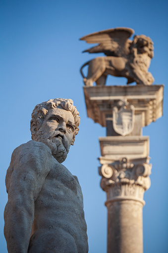 Statue of Caco the one present in the tenth labor of Hercules and in the back the column with a winged lion on square of liberty in Udine Italy