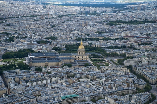 A panoramic aerial view of Paris skyline including river Seine lined with boats, a golden doom of Palace of invalides and other historical monuments, parks and gardens