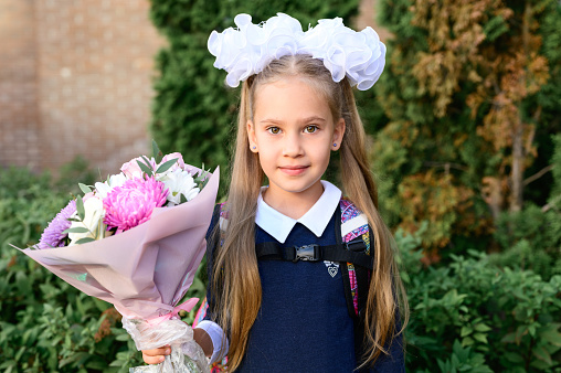 portrait of a cute little seven year old first-grader girl with a bouquet of flowers ready to go to school. back to school concept